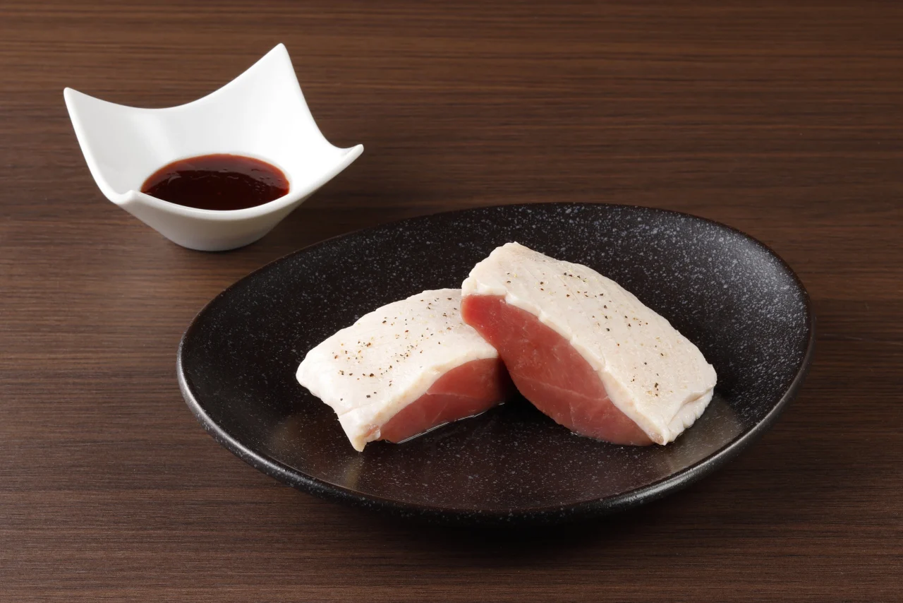 黒い皿に盛られた厚切りの鴨の王様ステーキと特製ソース