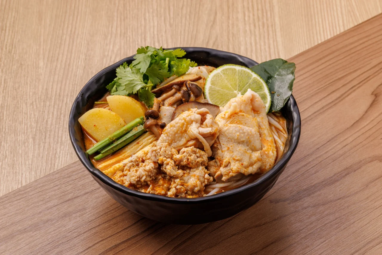 スパイシーココナッツカレー米線（鶏）。黒い器に鶏肉やライムなどを盛り付けた一杯