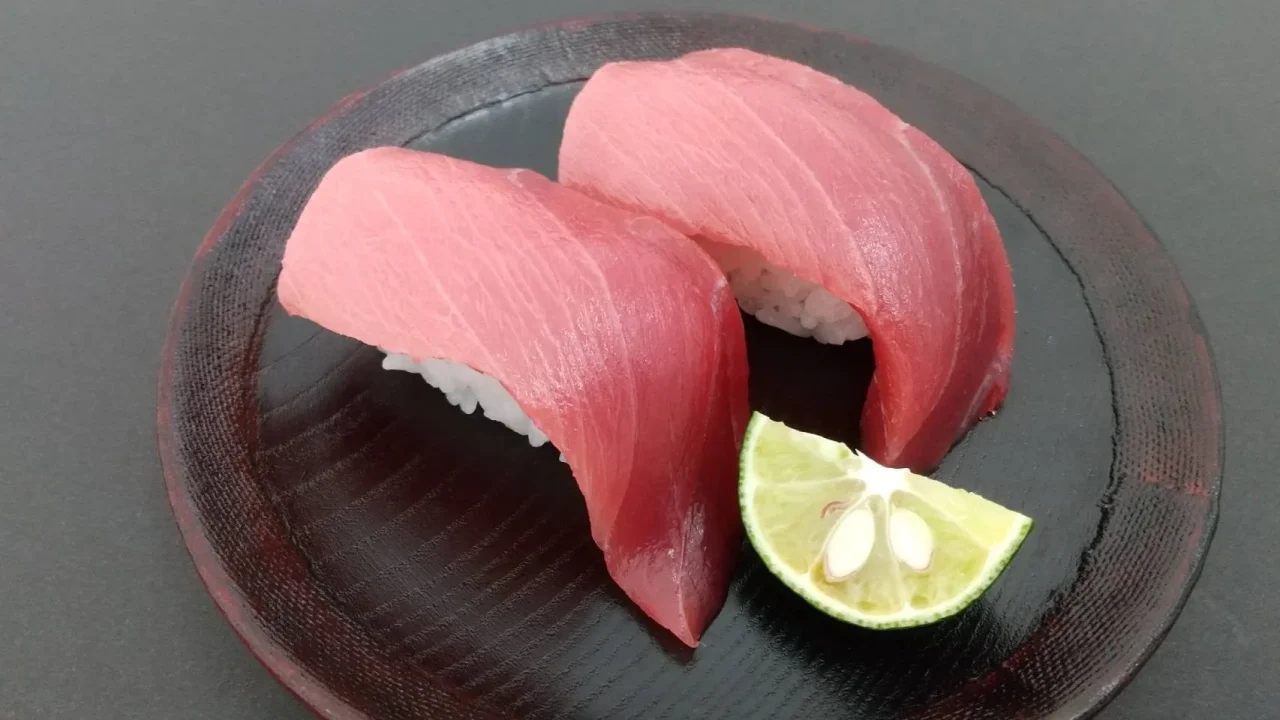 黒い皿に盛られた京まぐろのにぎり寿司2貫と柑橘のくし切り