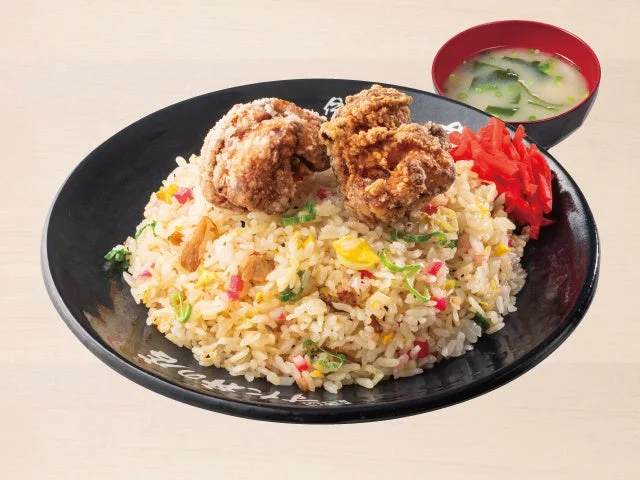唐揚げチャーハン。黒皿にチャーハンと唐揚げ2個、赤い細切り野菜、スープが添えられた一皿。