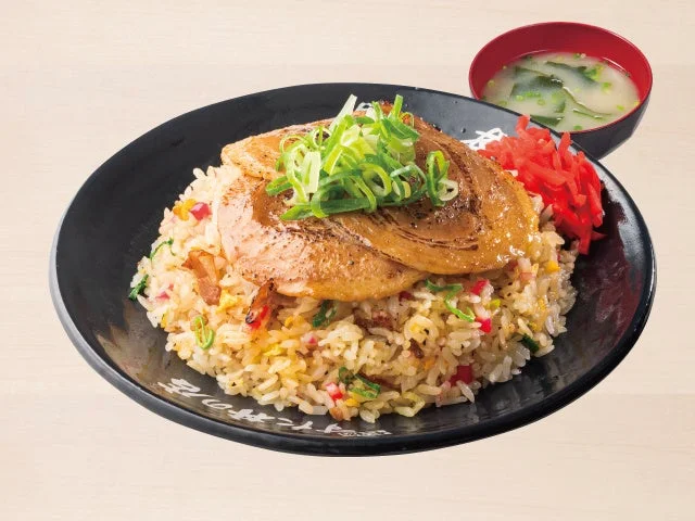 黒い皿にチャーシューをのせた焼豚チャーハンとスープ