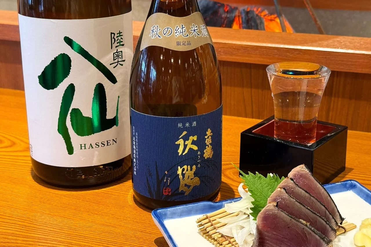 陸奥八仙 特別純米 緑ラベルのボトルと、隣に置かれた日本酒グラス、刺身盛り合わせ