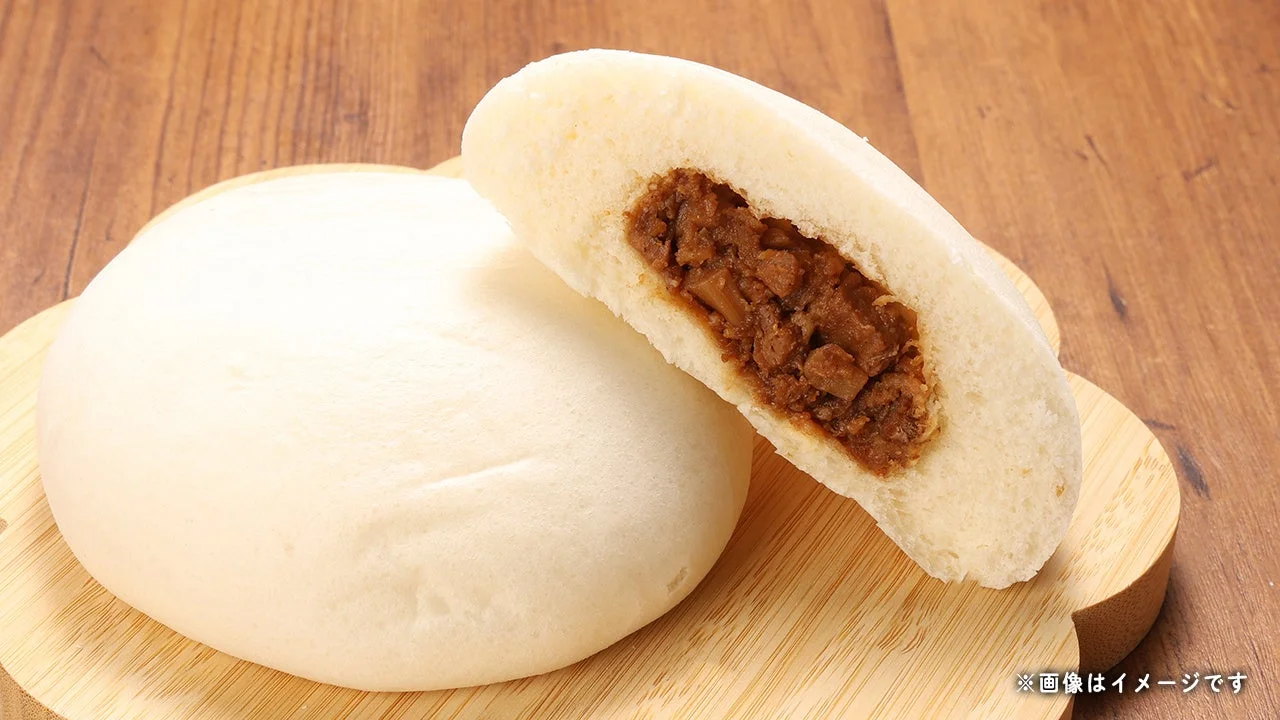 大きな麻婆肉まん。白い中華まんが木製プレートに置かれ、半分は切られて赤褐色の具材が見える。