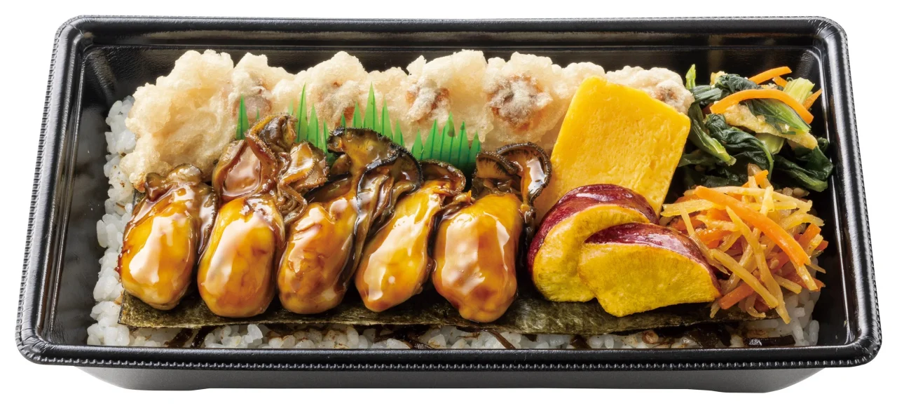 黒い容器に入った弁当で、ご飯の上に茹で牡蠣とカキフライ、野菜や卵焼きが乗っている