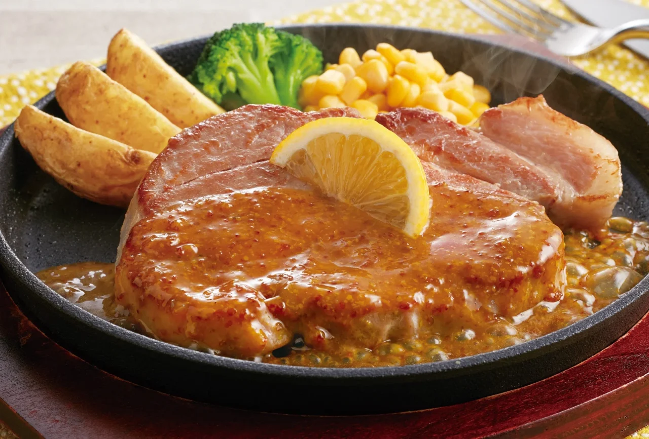 肉旨!厚切り豚肩ロースステーキ~ゴールデンマスタードソース。鉄板に盛られた豚ロース肉にマスタードソース、レモン、ポテト、ブロッコリー、コーンを添えた外観。