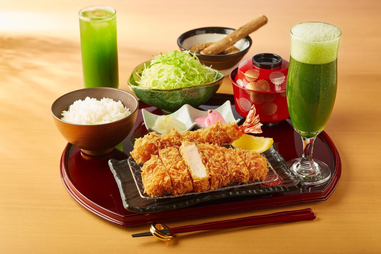 緑色のドリンク2杯と、かつ、ご飯、千切りキャベツを並べた食卓