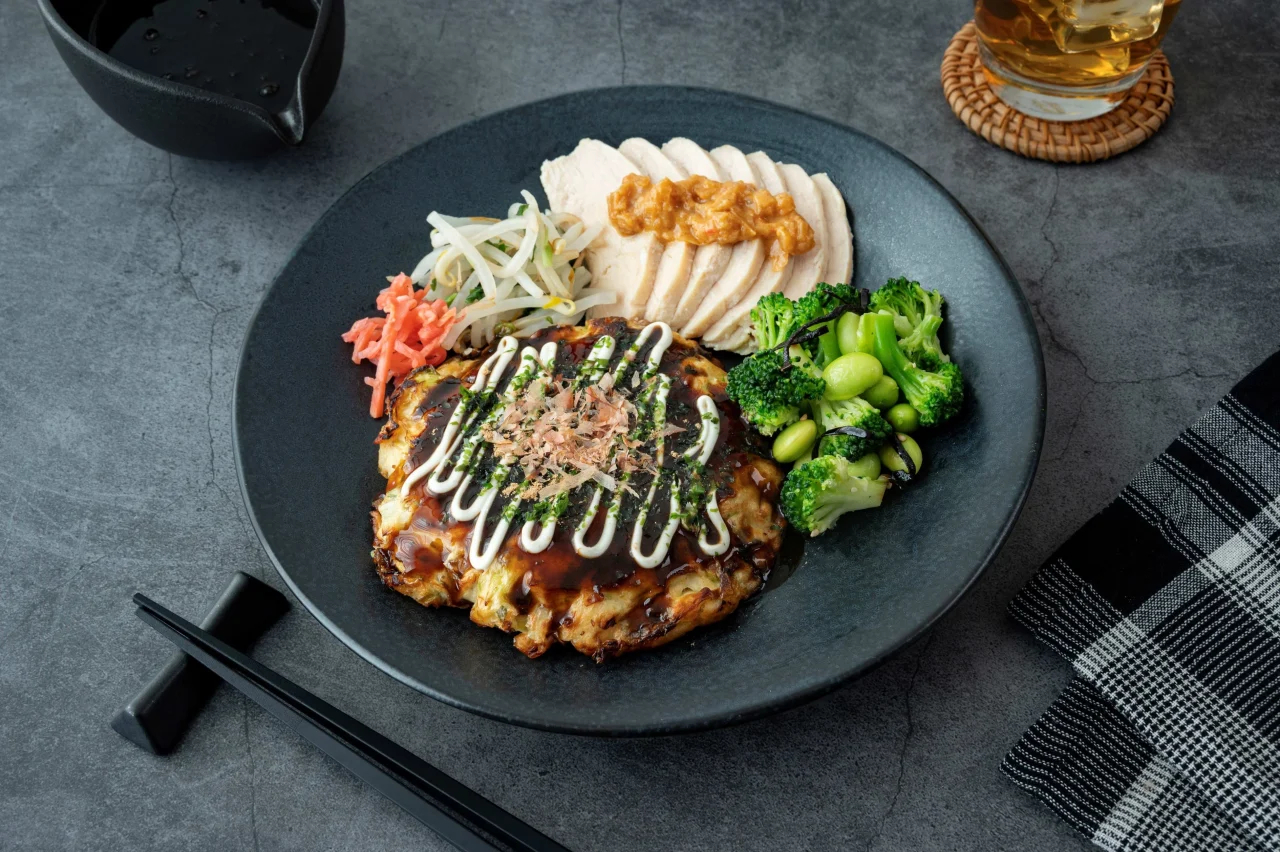 黒皿に盛られたお好み焼き、鶏肉の辛みそだれ、ブロッコリー