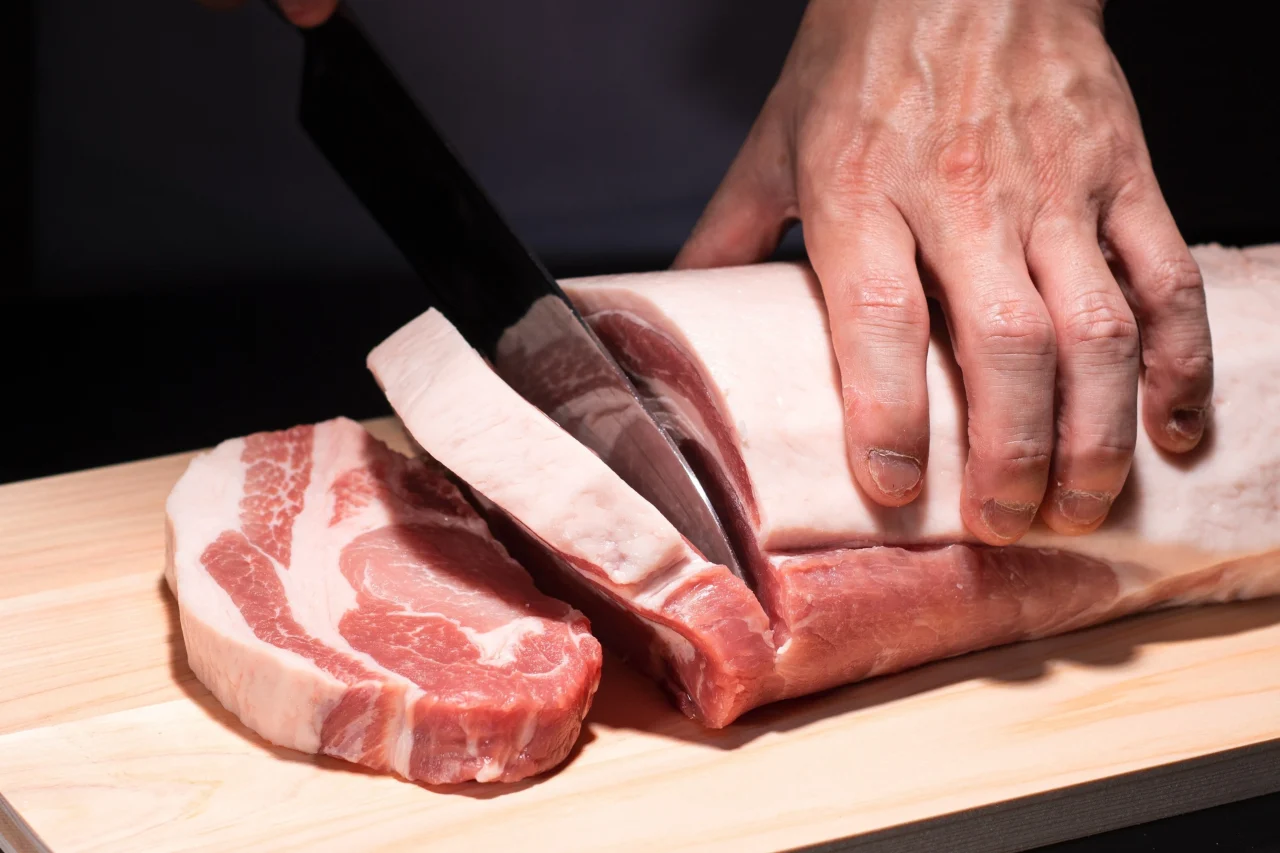 まな板の上で包丁で厚切りにされる、とんかつ用の厳選豚の塊肉