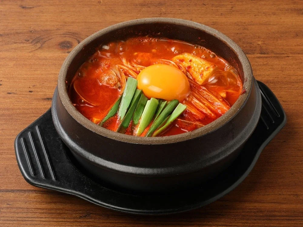 黒い石鍋に入った激辛チゲ。卵黄とニラがのった赤いスープ
