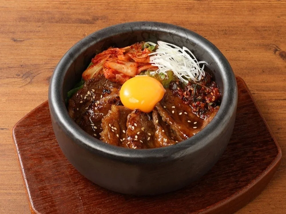 牛カルビ焼肉石焼ピビンバ。黒い石鍋に焼肉、キムチ、卵黄をのせた一品