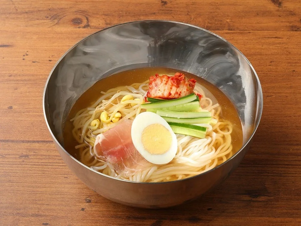 オリジナル冷麺。金属の器にキムチ、きゅうり、ゆで卵、もやしがのる
