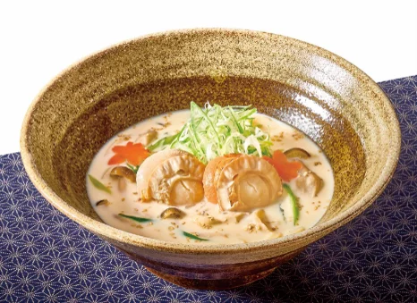 帆立のごま豆乳うどん。乳白色のスープに帆立と青ねぎをのせた茶色の鉢
