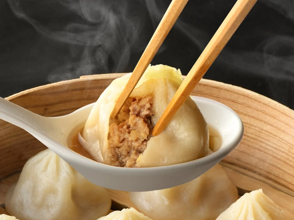 せいろの中の蒸し点心をレンゲに乗せ、箸で割って挽肉の餡が見える様子