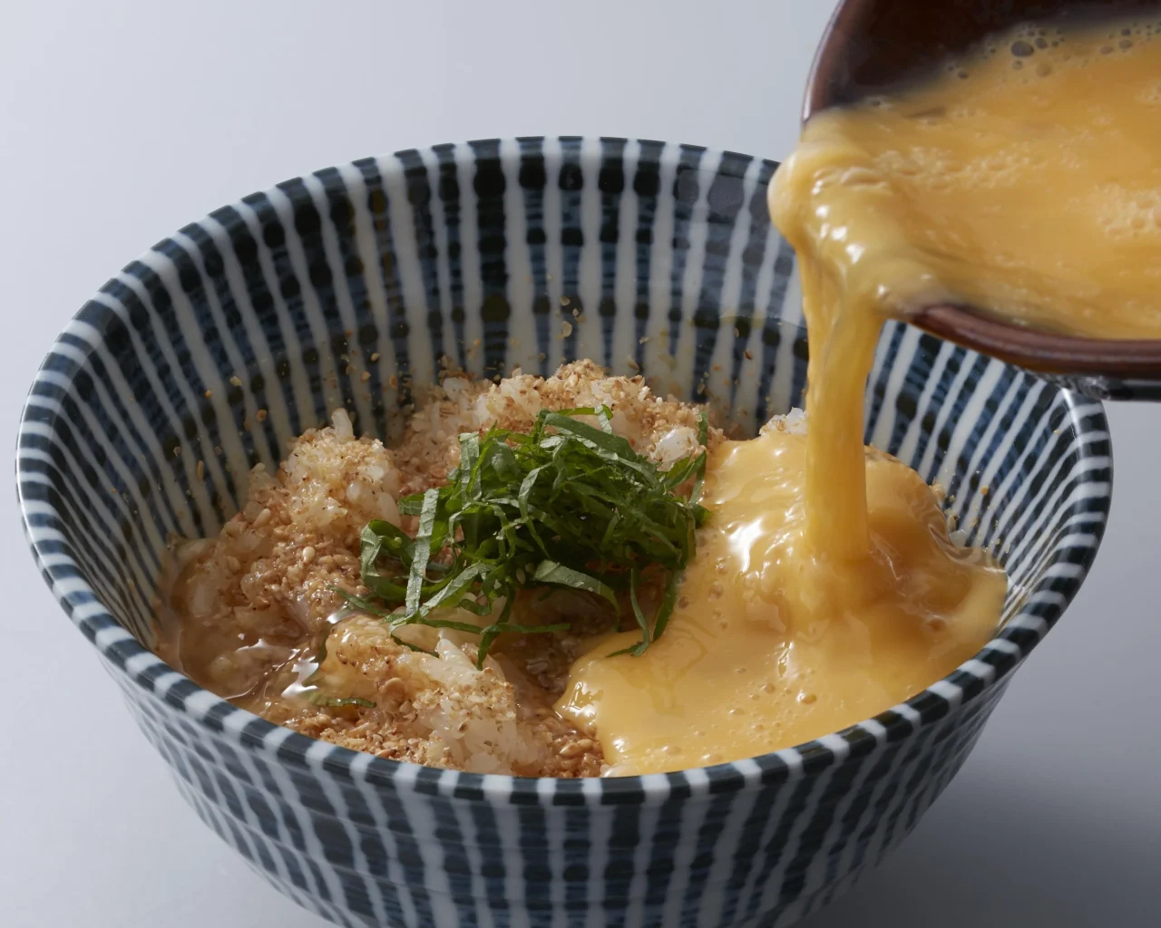 TKGG（たまごかけ胡麻ごはん）に溶き卵を注ぐ様子。大葉とごま入り