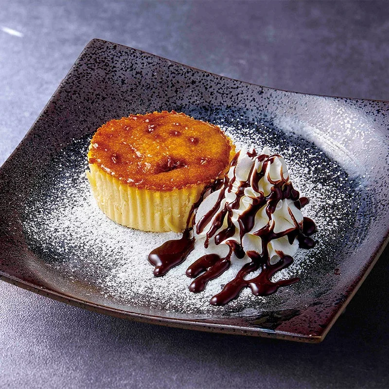 濃厚バスクチーズケーキ。黒い皿に粉糖、生クリーム、チョコソース添え