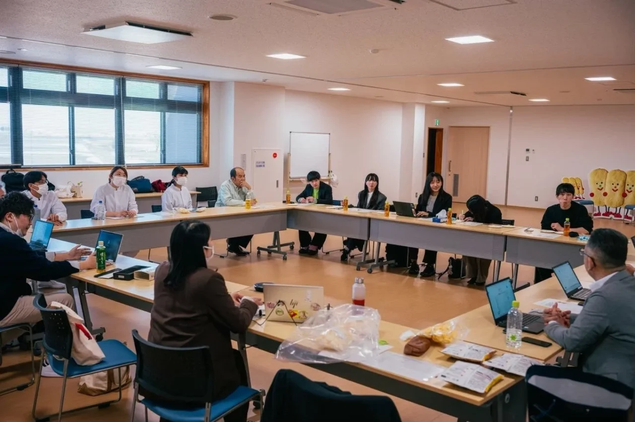 会議室でU字型に並んだ長机を囲み、ノートPCを使って話し合う参加者たち
