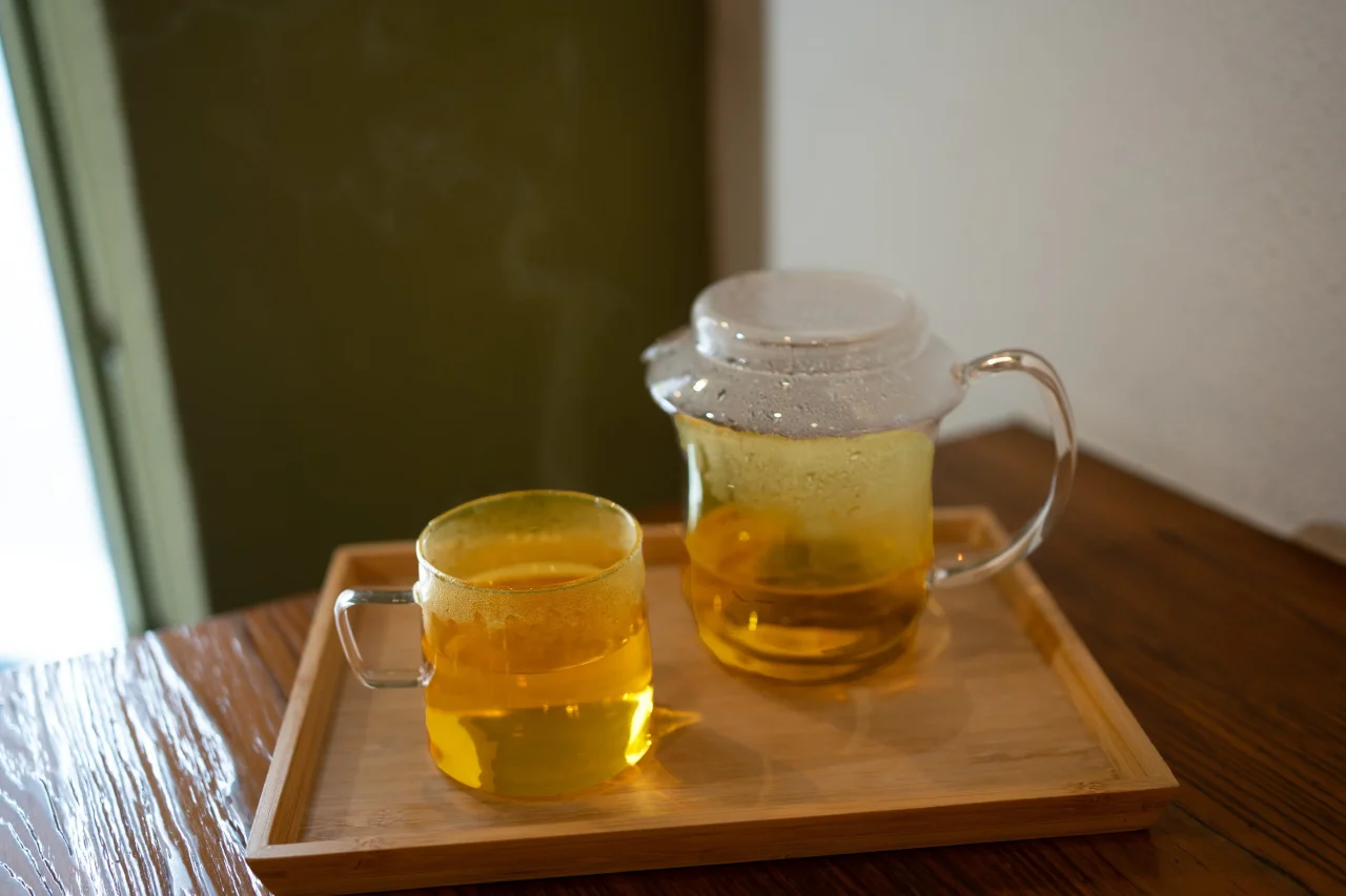 木のトレイに載った、黄金色のお茶入りガラスのカップとポット