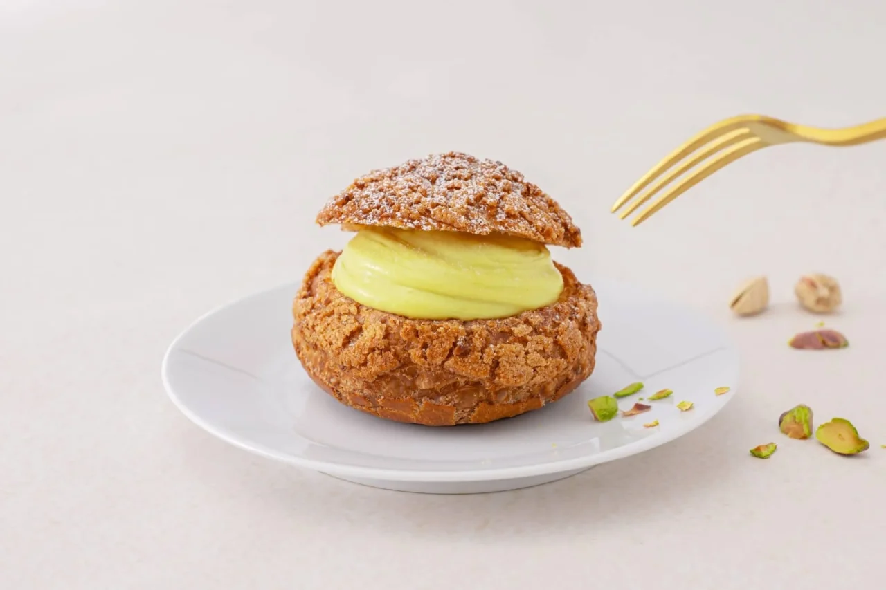 白い皿にのったピスタチオのシュークリーム。ピスタチオ色のクリームと砕いたナッツ