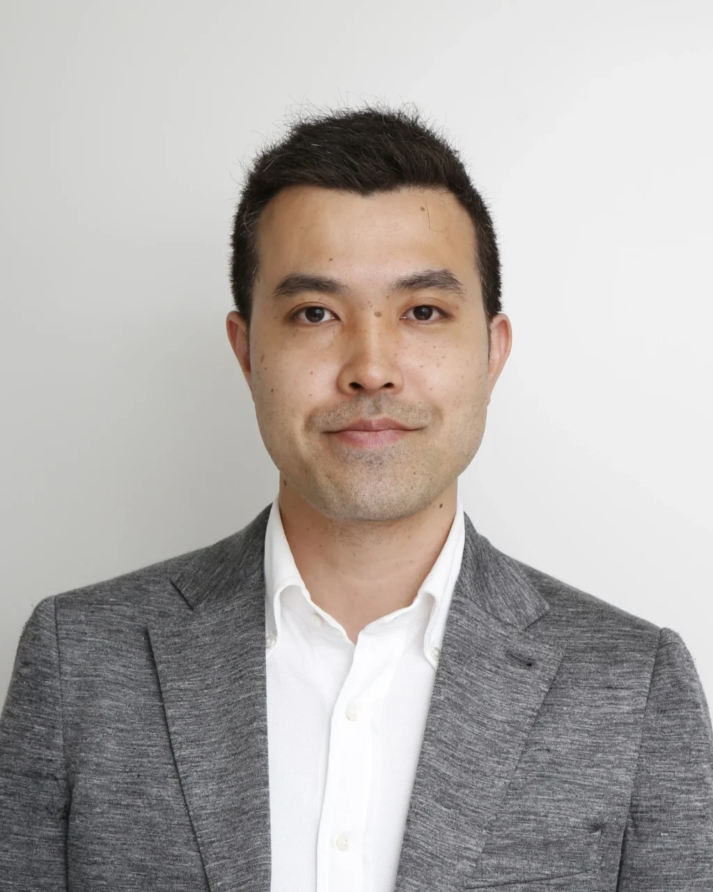成城石井 商品部 次長(バイヤー)坪井 元のポートレート。グレーのジャケットに白シャツの男性