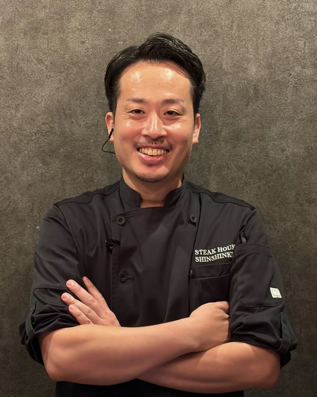 STEAK HOUSE SHINSHINKIEI 料理長 平原 惇也様。黒い調理服で腕を組む