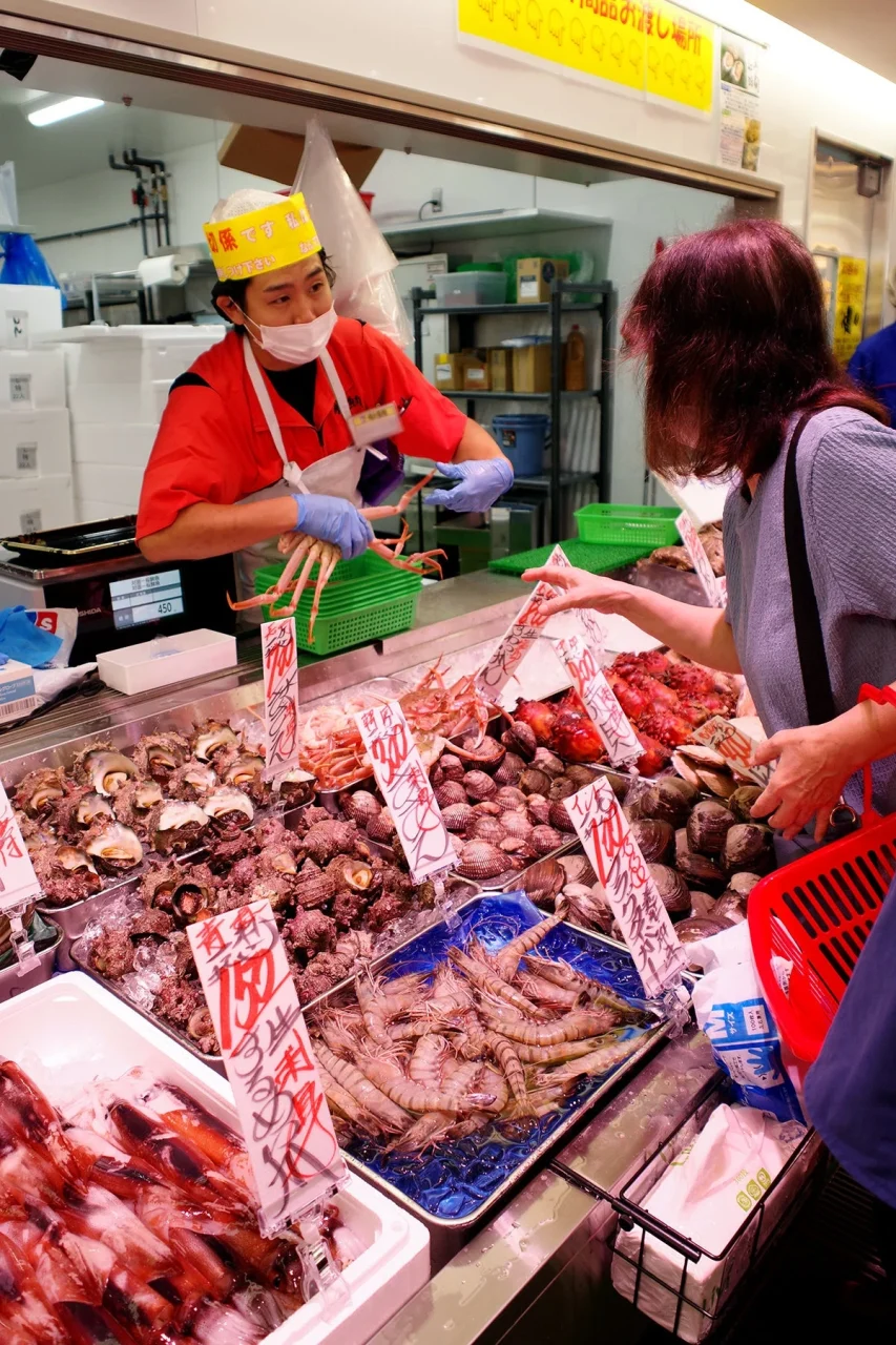 対面売場で黄色い帽子の店員が客に鮮魚を見せている様子