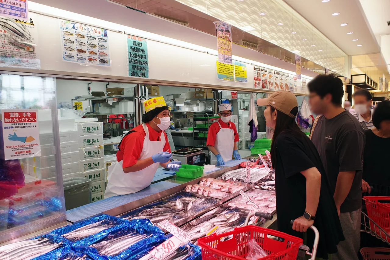 対面売場で鮮魚を前に接客する店員と買い物客