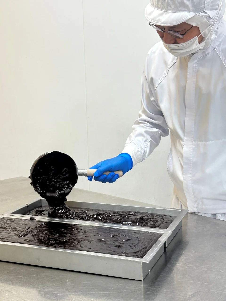 中田屋の製造現場で、黒い餡状の生地を容器に流し入れる作業者