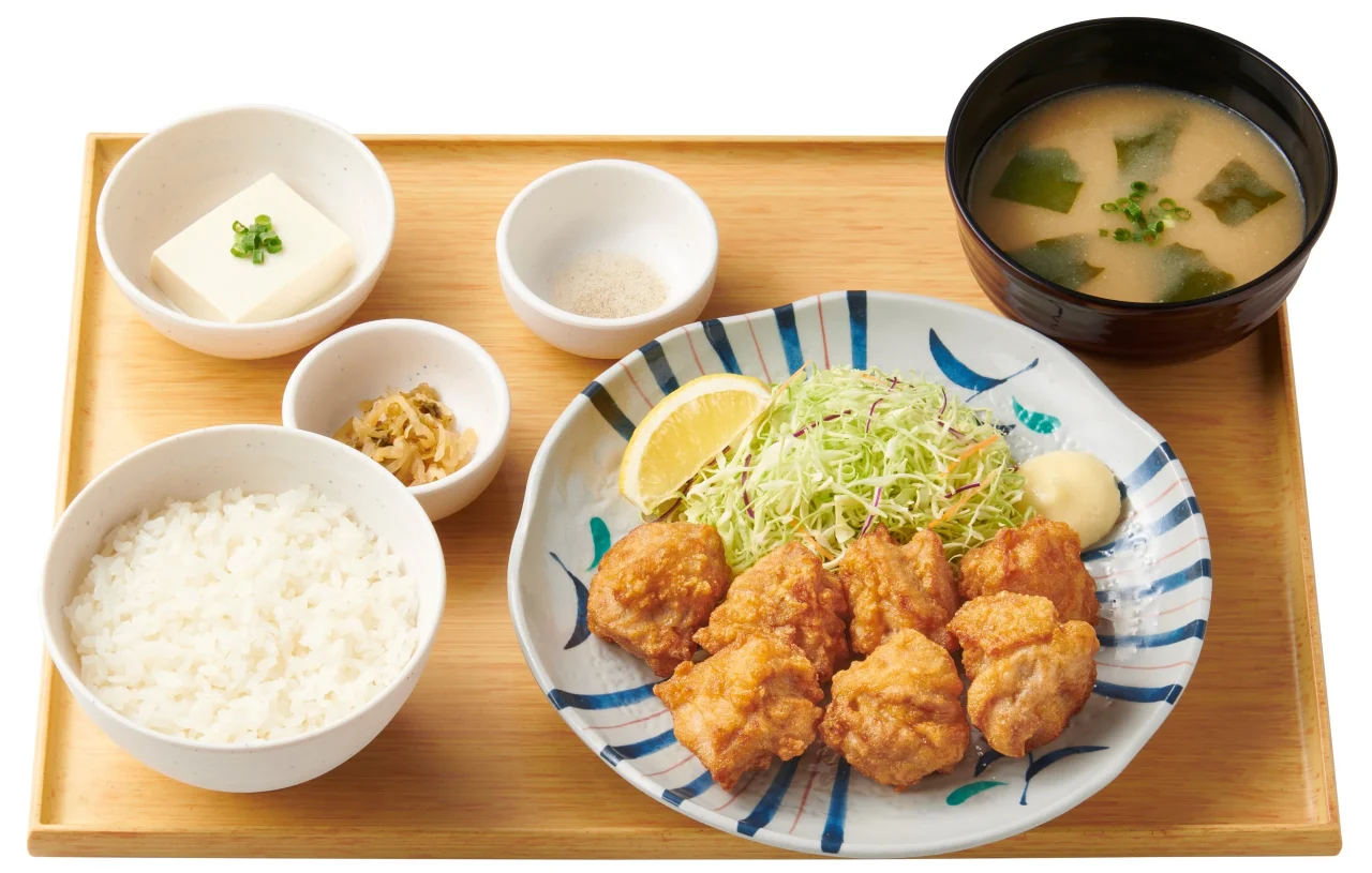 から揚げ定食。から揚げ、キャベツ、レモン、ご飯、味噌汁、小鉢を木製トレーに並べた様子