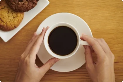 白いカップに入ったブラックコーヒーを両手で持つ様子とクッキー