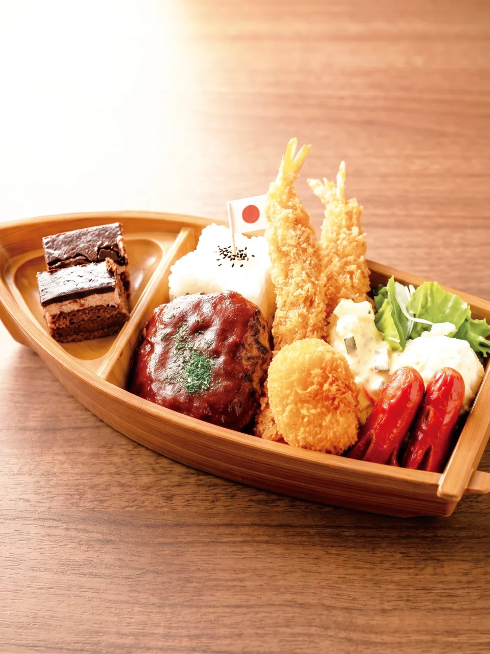 お子様セット。船形の木製容器にハンバーグ、エビフライ、ご飯、ソーセージ、ケーキを盛り付け