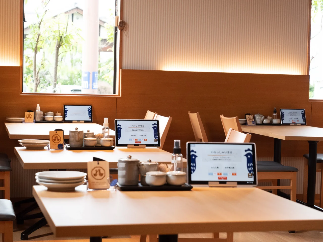 木目調の店内のテーブル席に、タブレット端末と調味料入れ、取り皿が並ぶ様子
