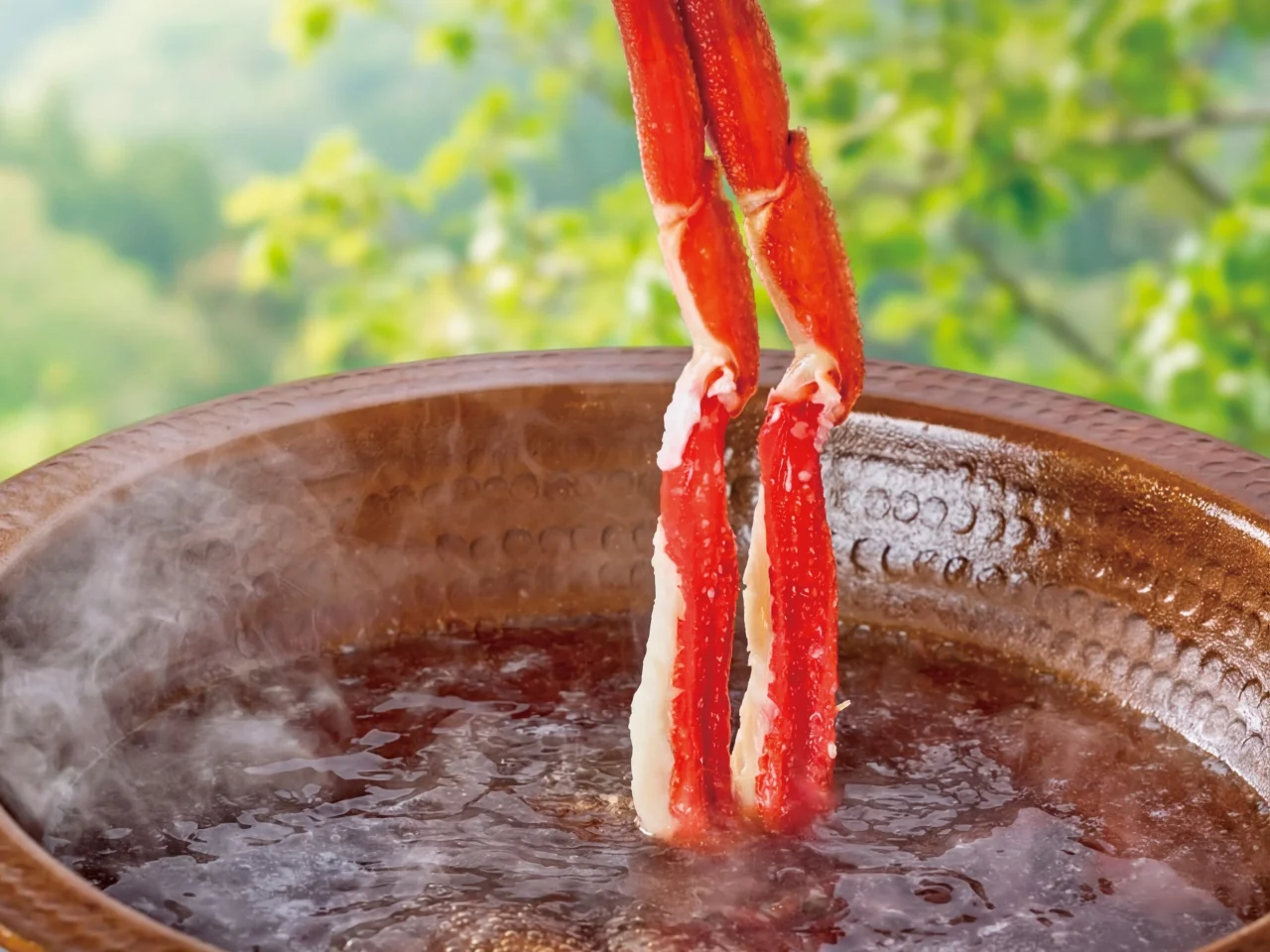 出汁にくぐらせるかにしゃぶのずわい蟹の身と湯気の立つ銅鍋