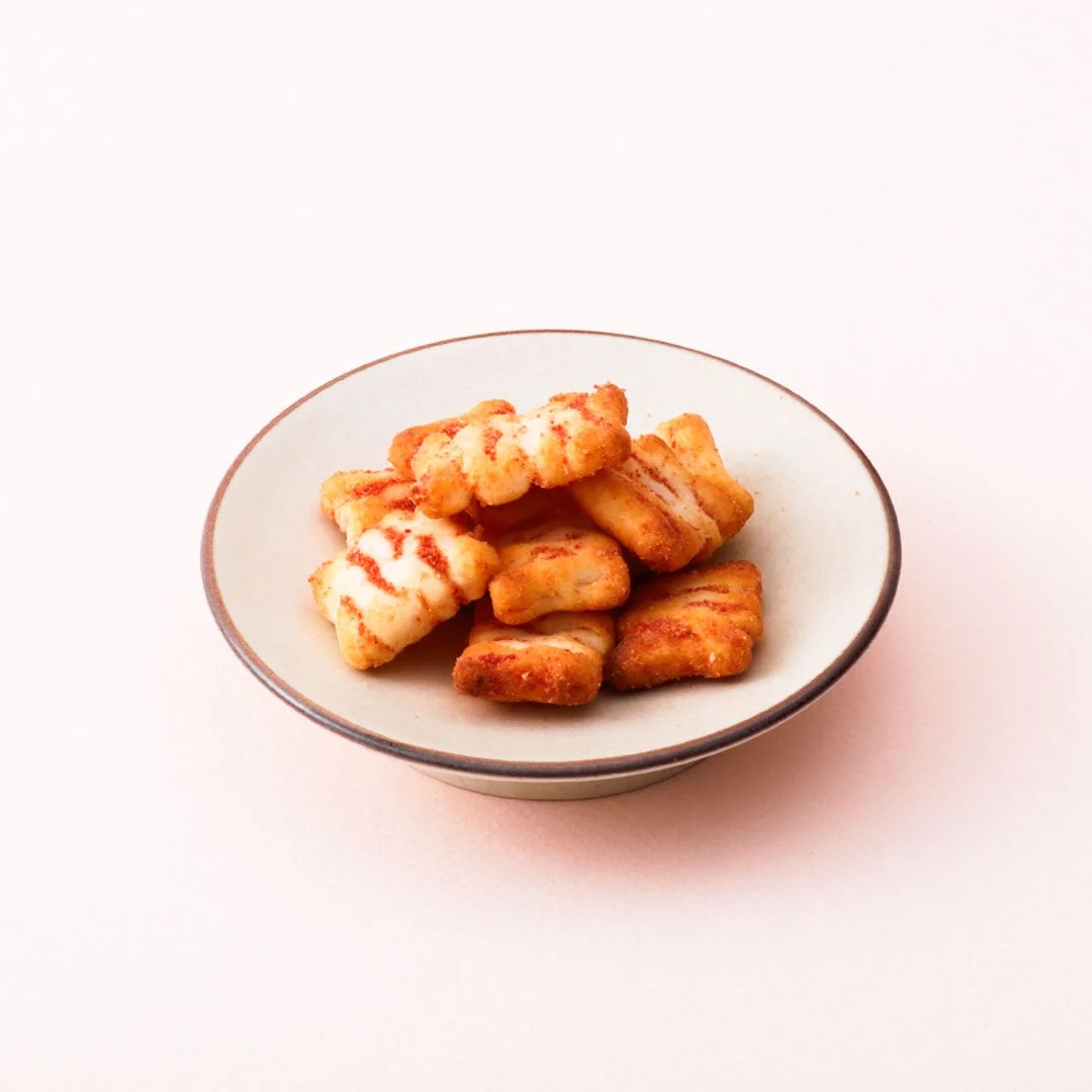 明太チーズおかき。白い小皿に盛られた、赤い味付けと白い模様のおかき