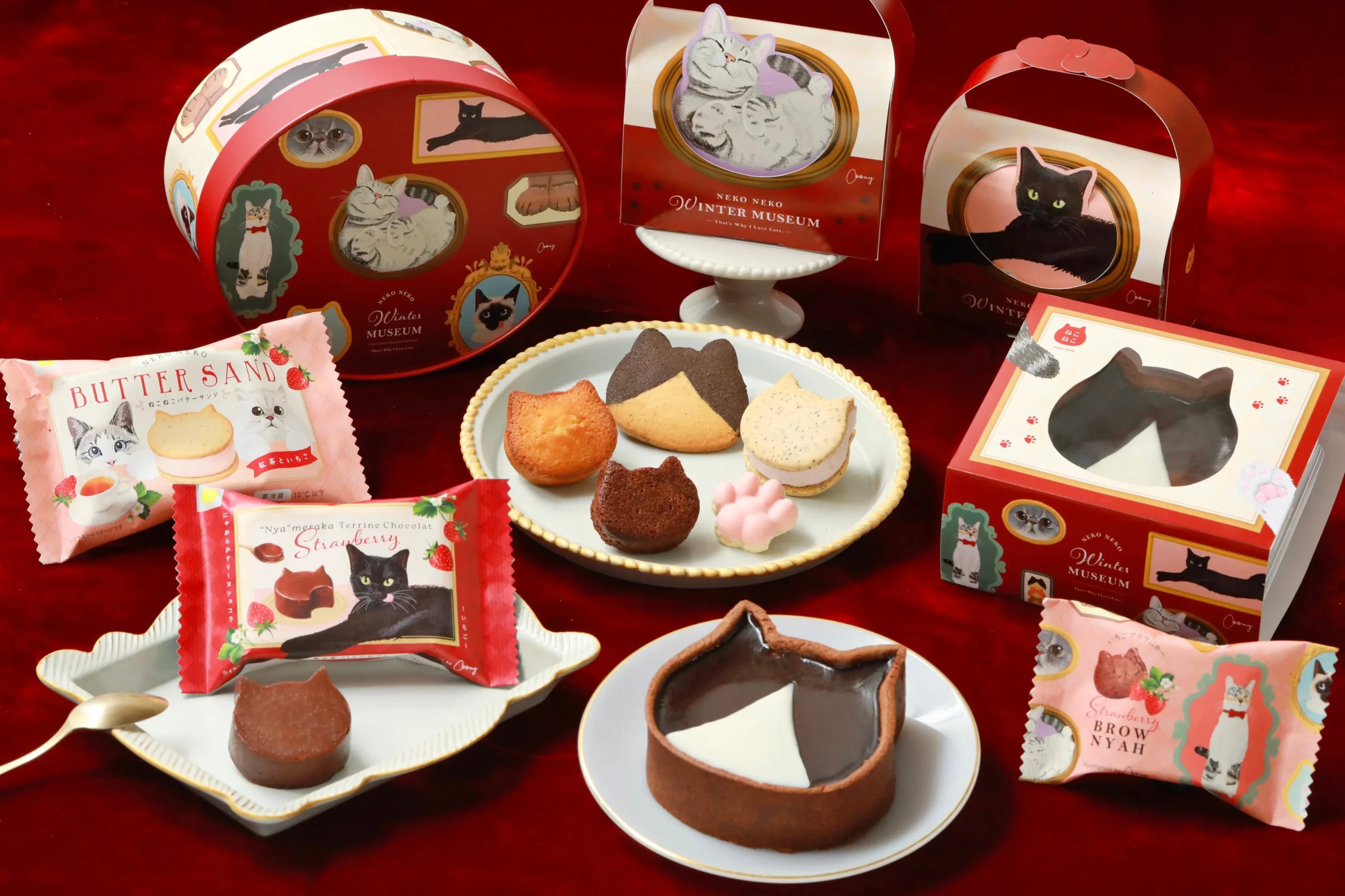 ねこねこウィンターミュージアムの新作スイーツとねこ柄パッケージが赤い布の上に並ぶ