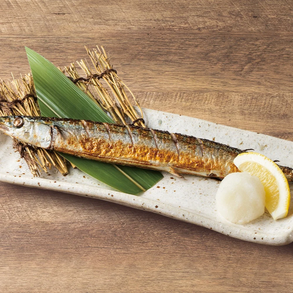 笹の葉を敷いた長皿の焼き魚とレモン、白い添え物