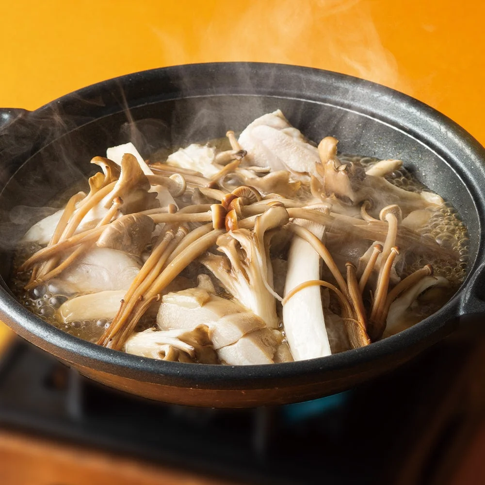 湯気の立つ黒い陶板鍋で調理中のきのこと鶏肉