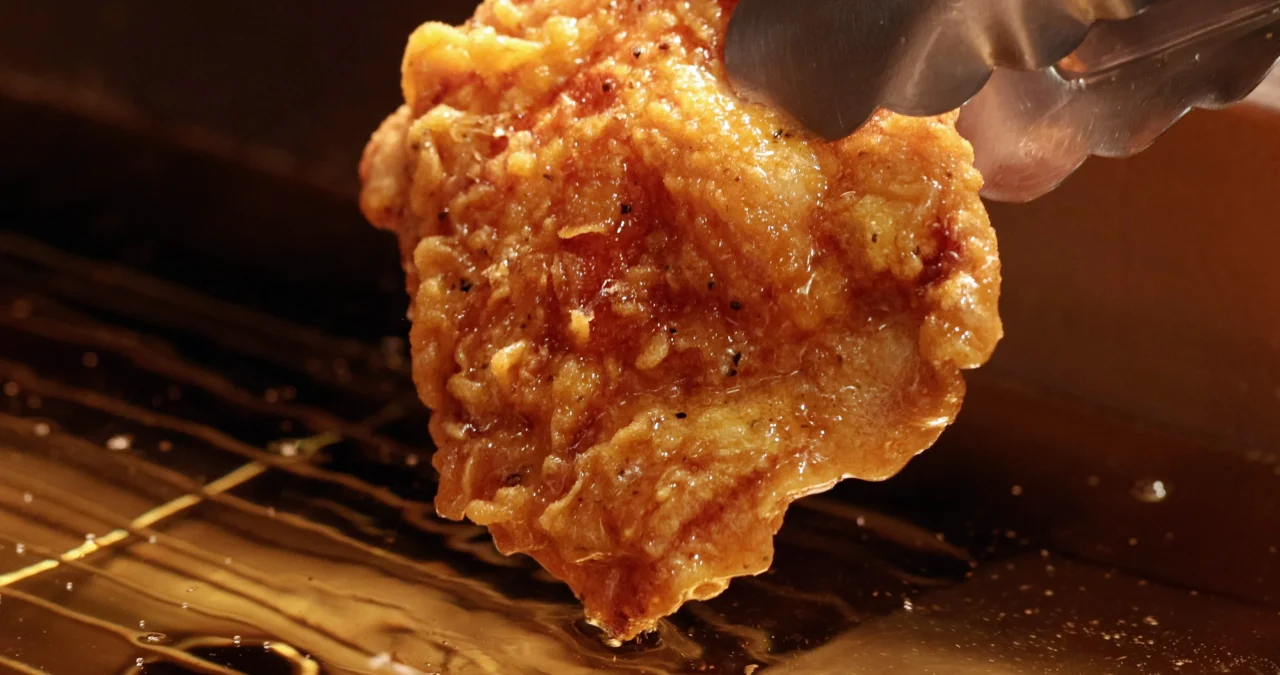 トングで持ち上げた、若鶏の上もも肉（サイ）のフライドチキン