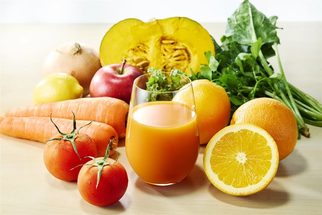 オレンジジュースのグラスと、野菜や果物が並ぶ様子