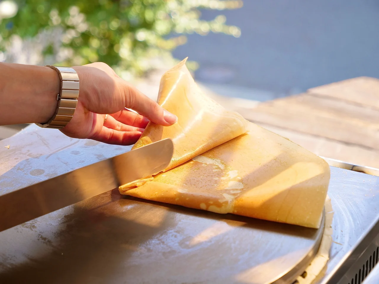 鉄板の上で焼いたクレープ生地をナイフで持ち上げ、手で折る様子