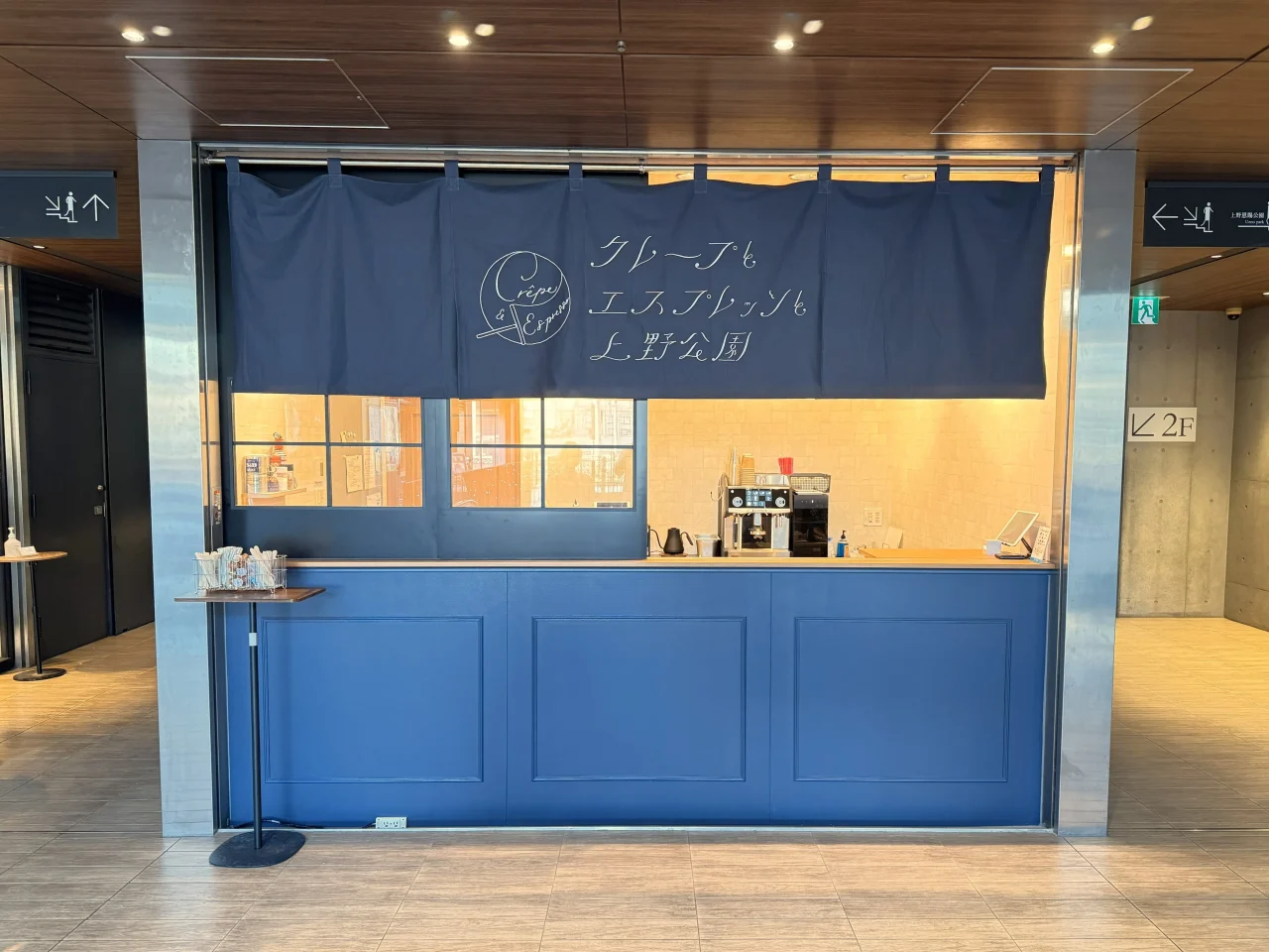 「クレープとエスプレッソと 上野公園」の紺色のれんと青い木製カウンターの店舗
