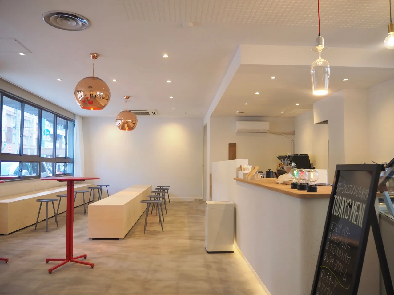 木目調のカウンターと赤いテーブル、銅色のペンダント照明がある店内