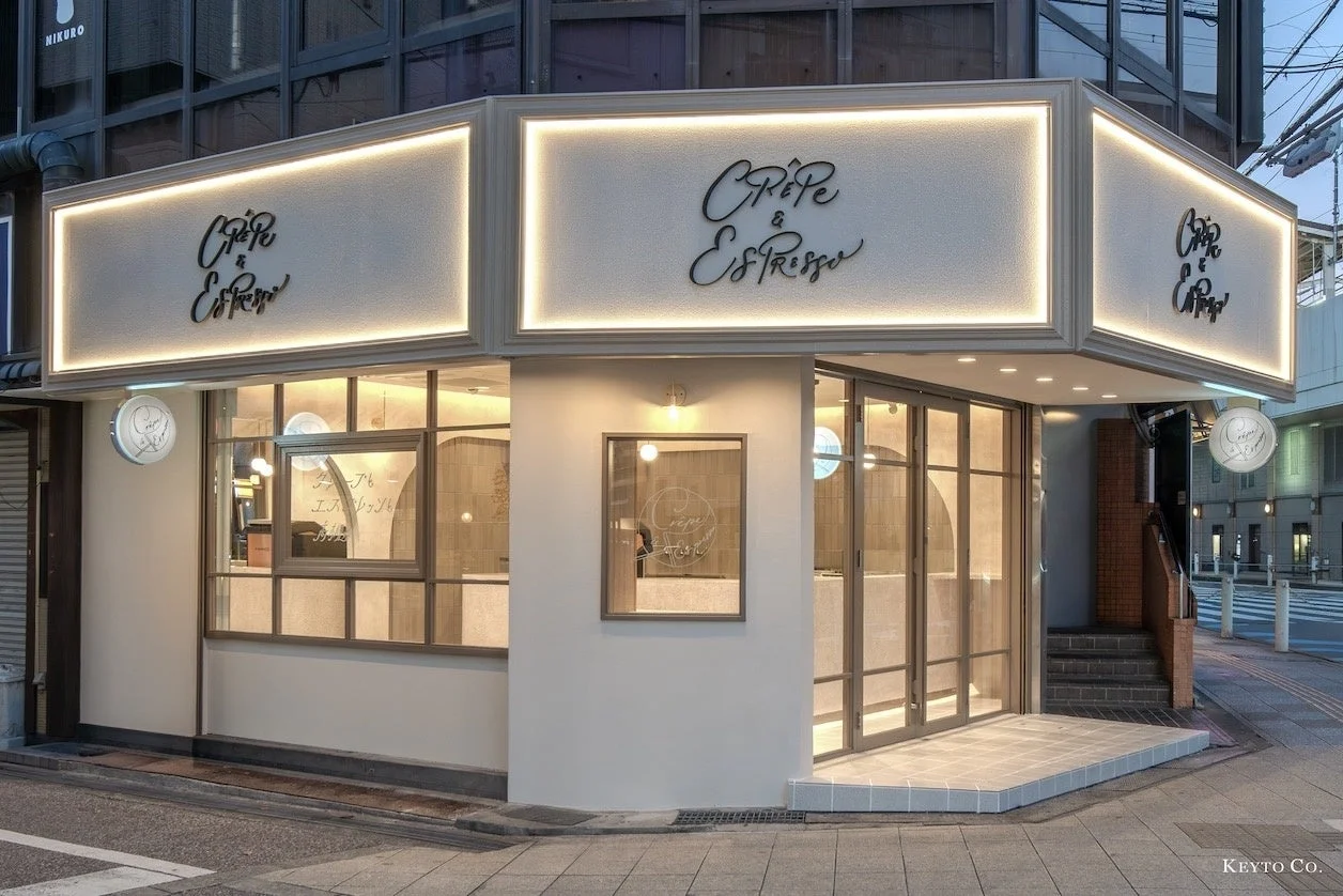 クレープ店の角地の路面店舗外観。白い壁と光る看板、ガラス扉
