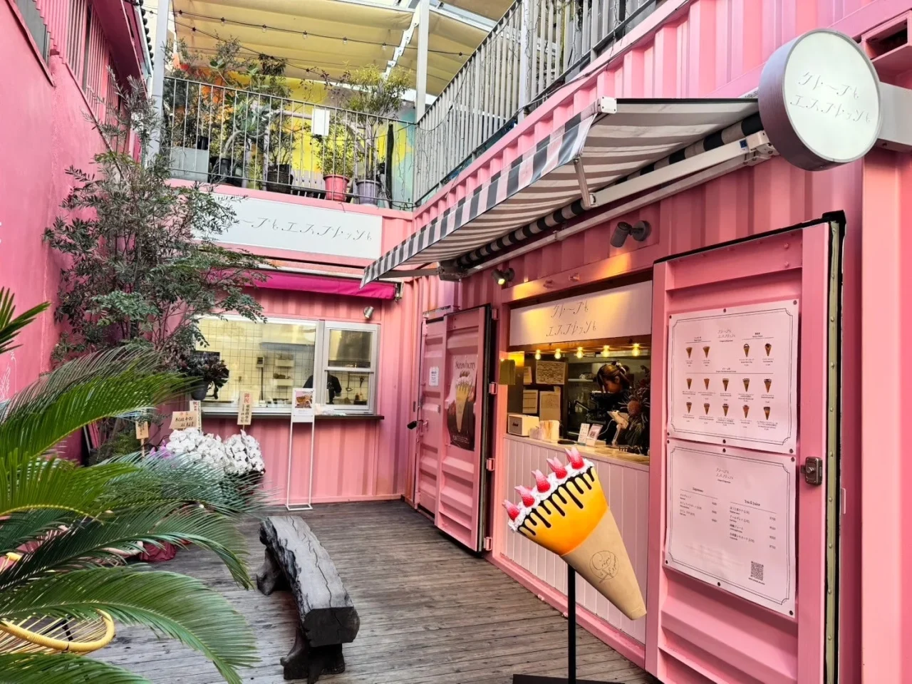 ピンク色のコンテナ造りのクレープ店の外観とクレープ形の看板