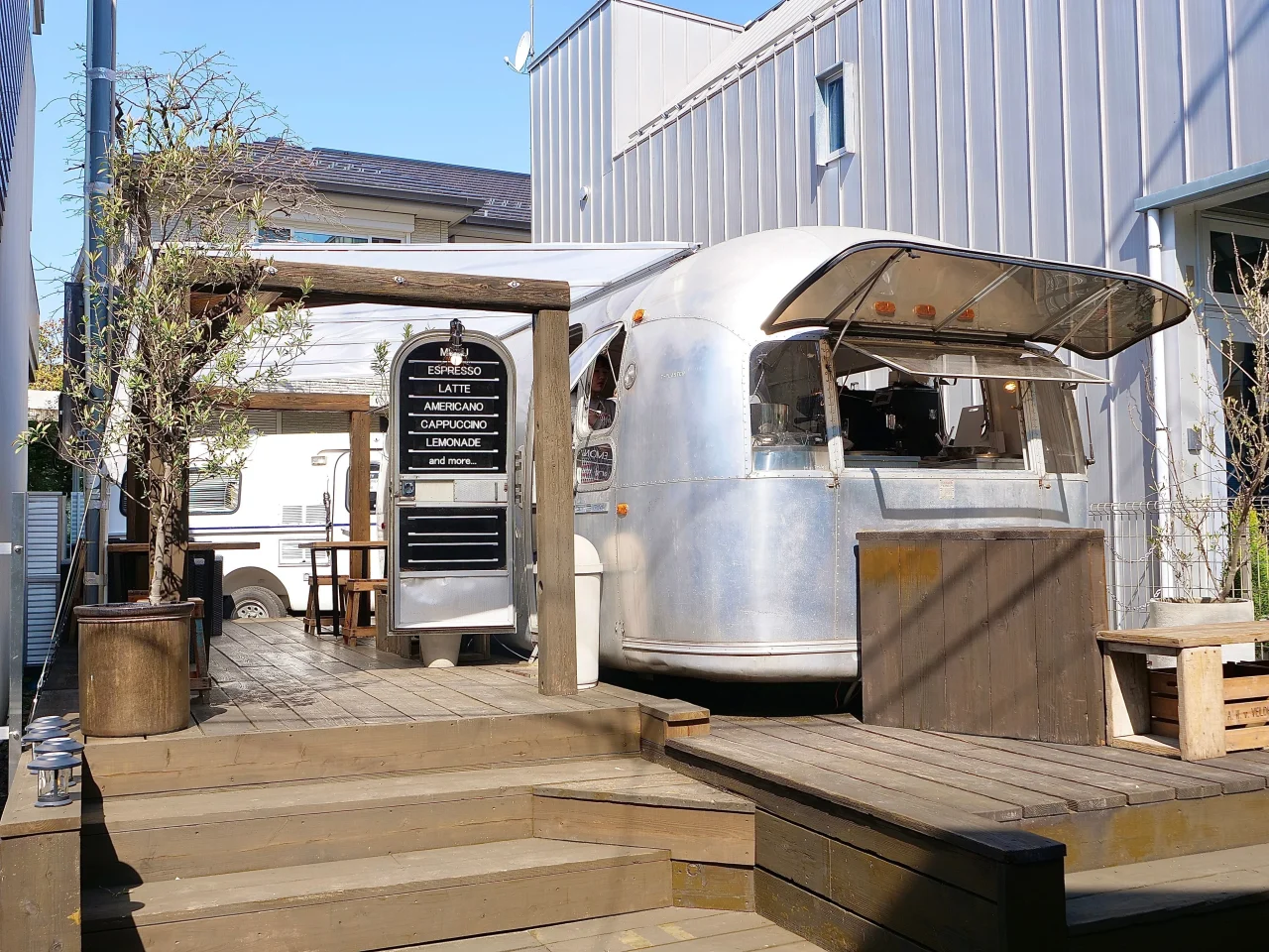木製デッキ上に停まる銀色のトレーラー型カフェとメニュー看板