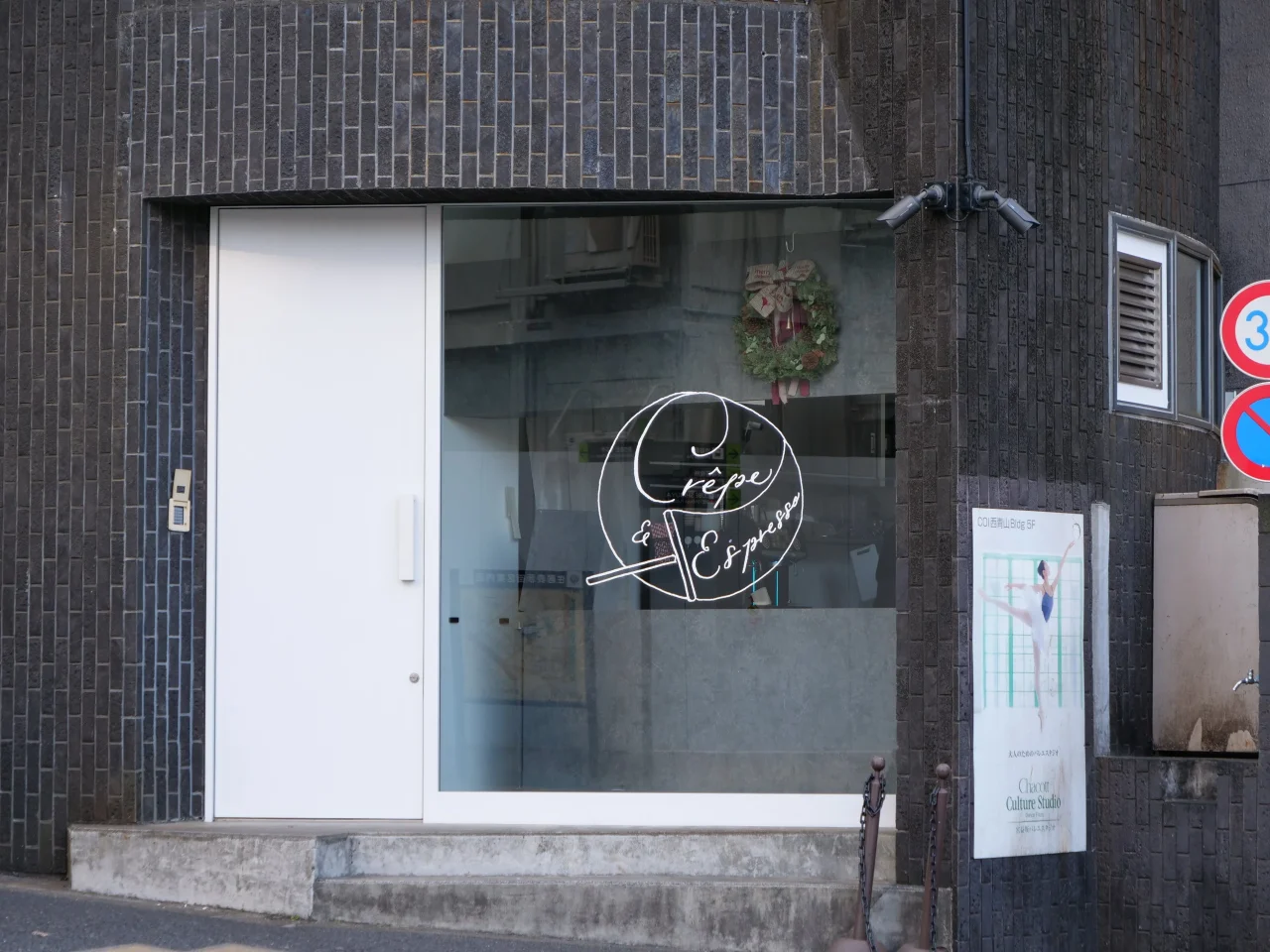 ガラス窓にロゴが描かれた、濃色タイル壁の店舗入口の外観