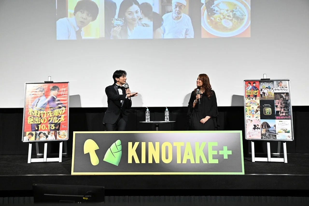 「KINOTAKE+」看板の前でマイクを持ち話す男性と女性のステージ