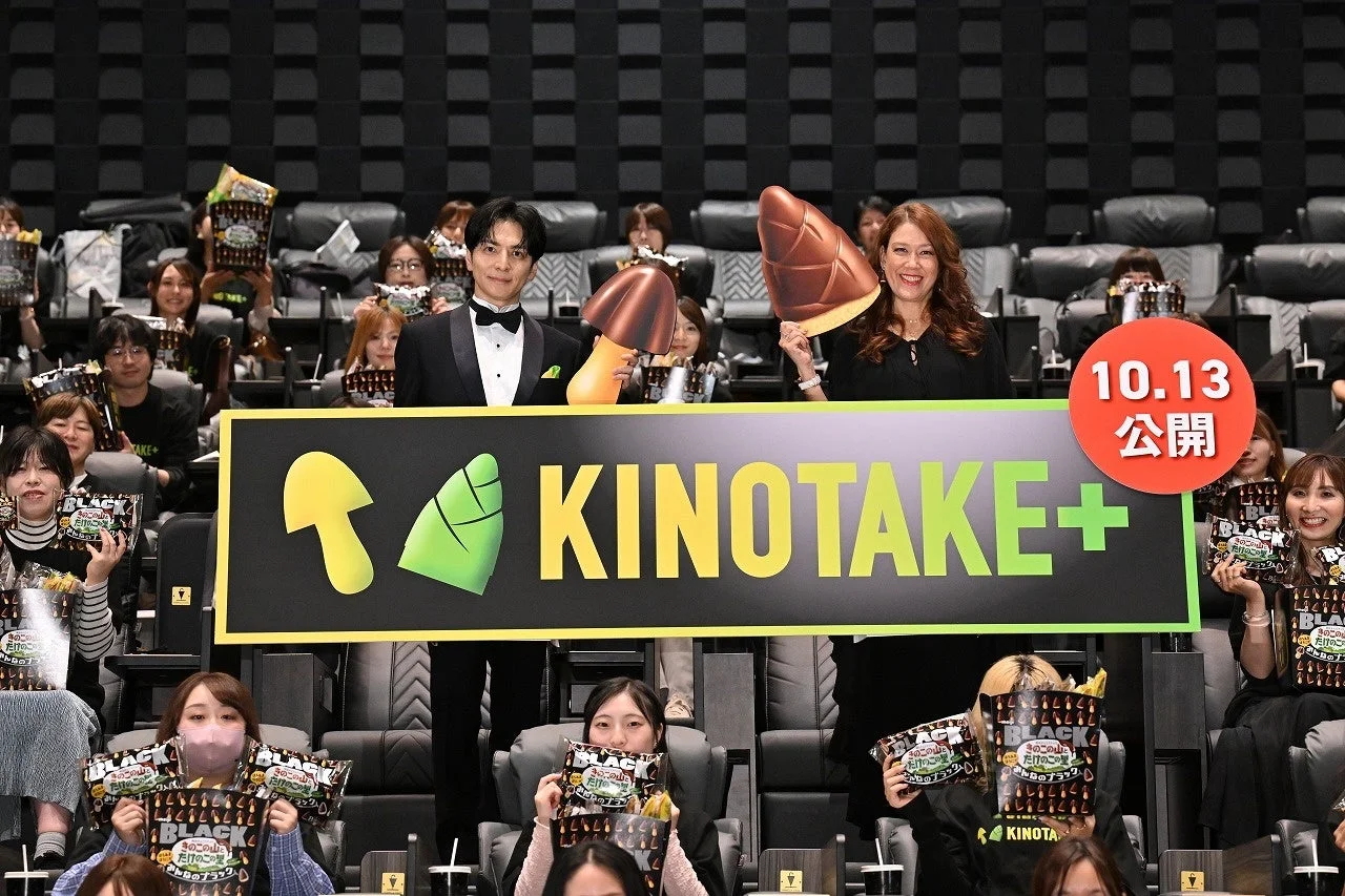 KINOTAKE+の看板を持つタキシード姿の男性とドレス姿の女性、客席のファン