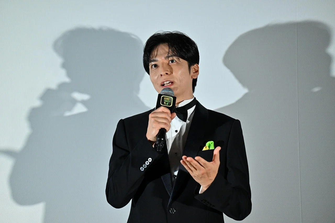 タキシード姿でマイクを持ち話す生田さん