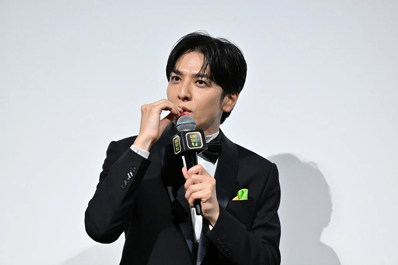 タキシード姿でマイクを持ち、口元に手を当てる生田斗真さん