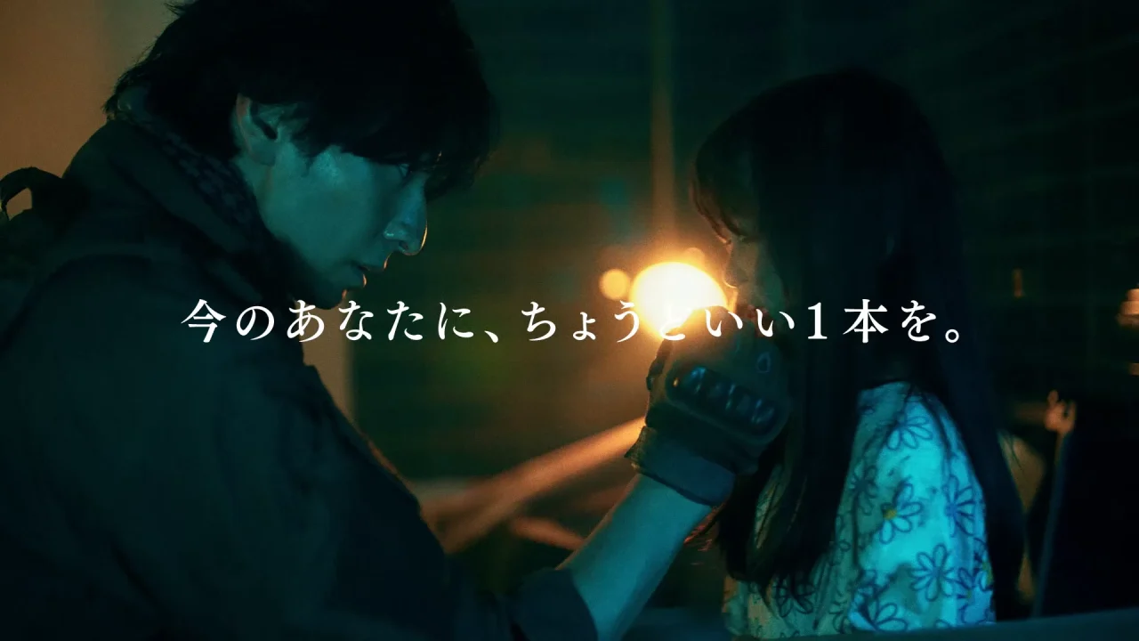 暗い場所で男性が手袋をした手で女性の顔に触れる映像。中央に字幕